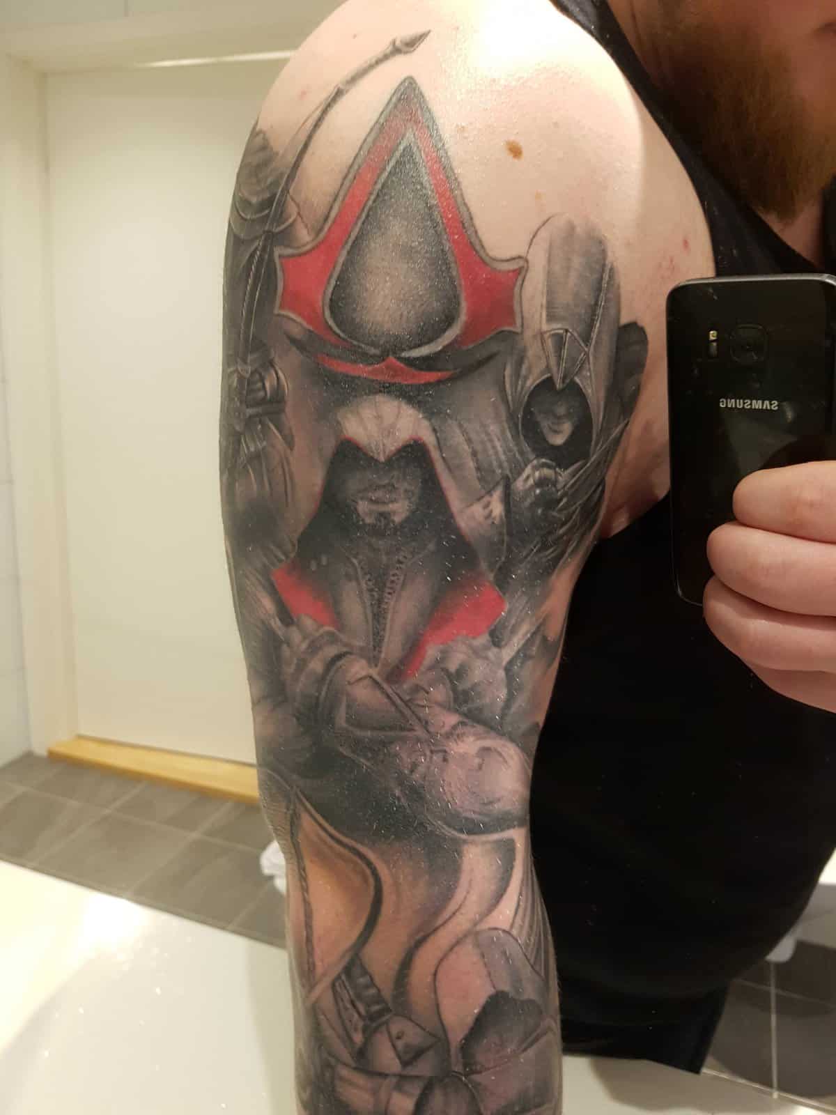 Kolorowy półrękaw Assassin’s Creed z czerwonym logo Kolorowy tatuaż Assassin’s Creed z czerwonym symbolem i zakapturzonymi postaciami na ramieniu