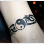 Tatuaż yin-yang na nadgarstku z tribalowym wzorem po bokach.
